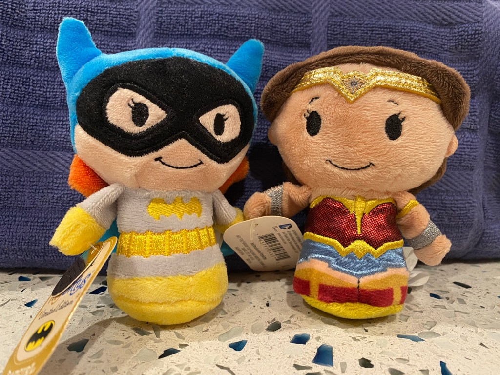 A close-up of two Itty Bitty dolls: Batgirl and Wonder Woman.