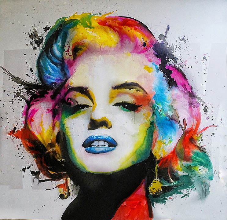 A close-up of Marilyn Monroe's face in full glamour mode, but with the black & white tonailty overlaid with bright, bold, unrealistic colors (blue lips, rainbow hair, pitch black and red diagonal neck)