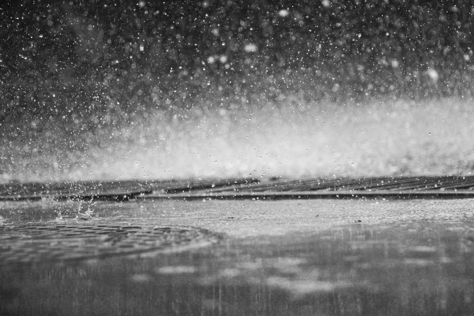 Closeup photo in black & white of rain hitting street pavement, including a manhole cover.