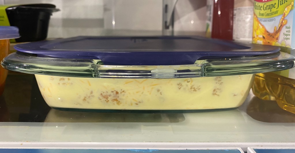 A pyrex casserole dish sitting on a refrigerator shelf.