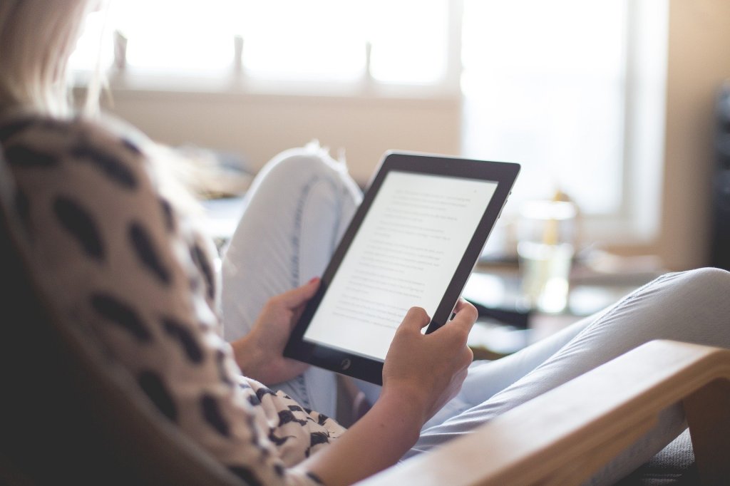 A soft focus shot, looking over the shoulder of a white, female-presenting human at the Kindle she is reading.