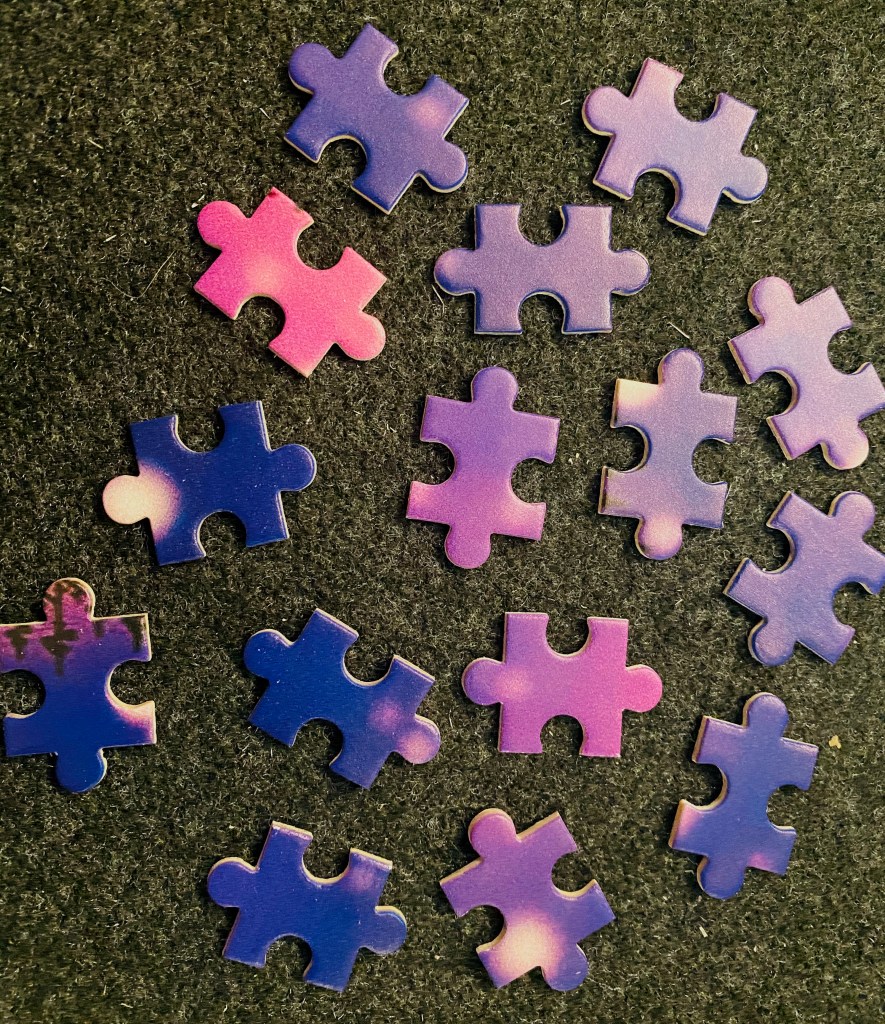An arrangement of puzzle pieces, all the same shape and in slightly different shades of purple and magenta.