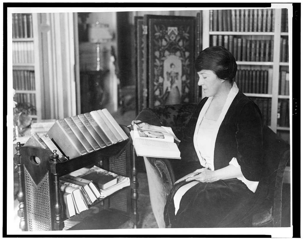 Black & white photo of mystery author Mary Roberts Rinehart reading a book in what appears to be a home library or study.